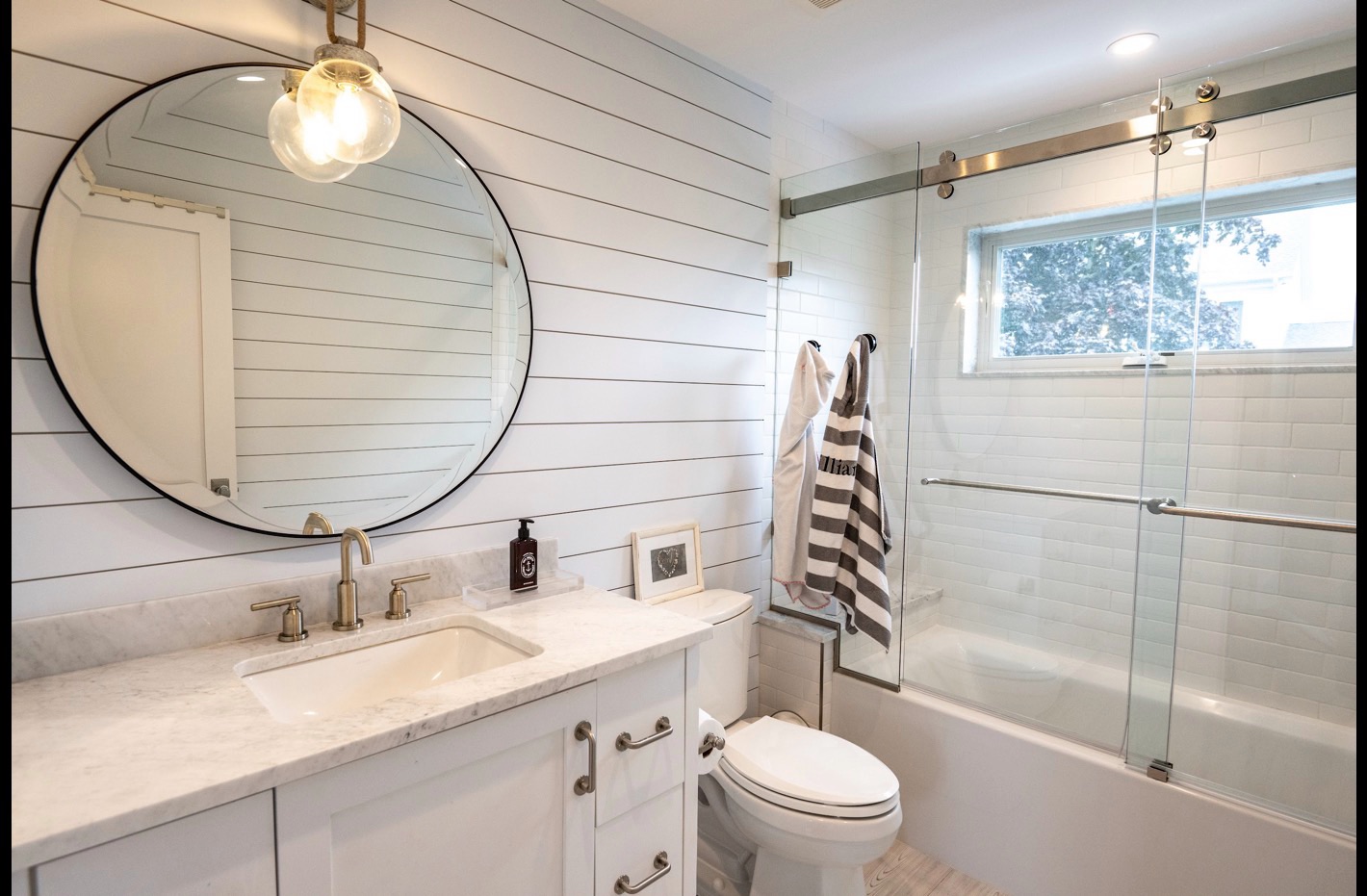 White bath with shiplap walls and a round mirror