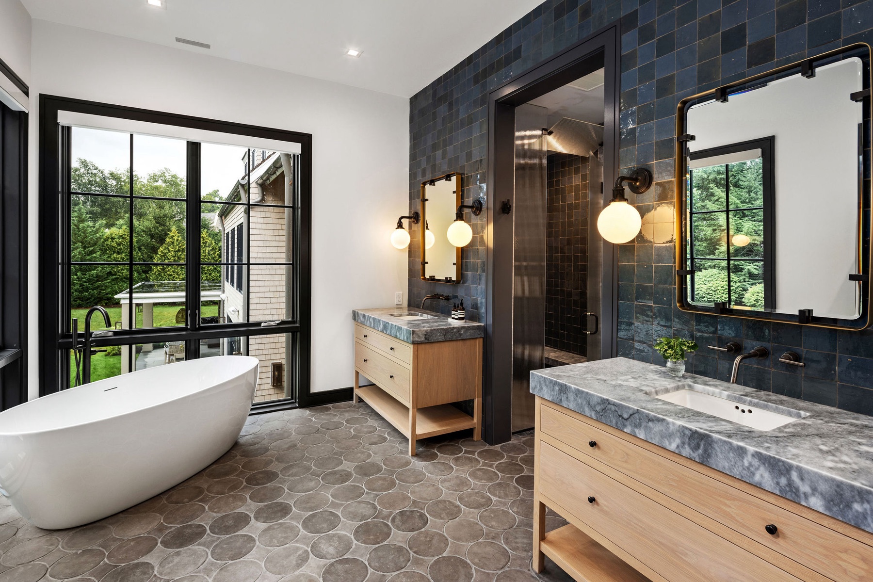 Master bath with a tub against dark tile and steel windows