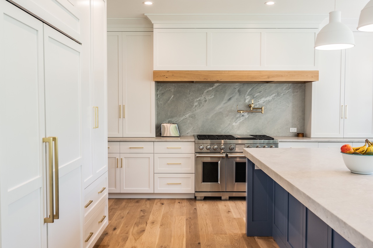 White kitchen with a stone hood and brass pulls